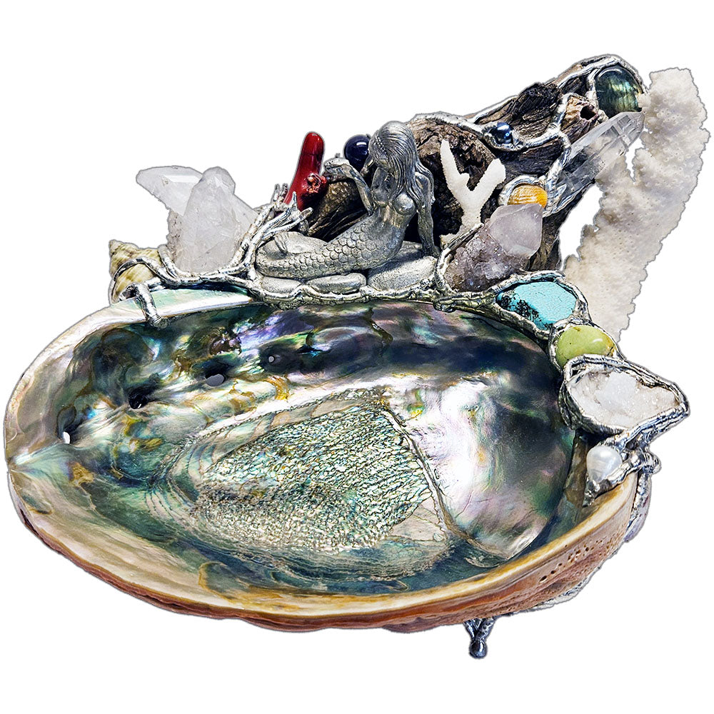 A mermaid rests on a large pink abalone shell, adorned with corals, seashells, gemstones and driftwood