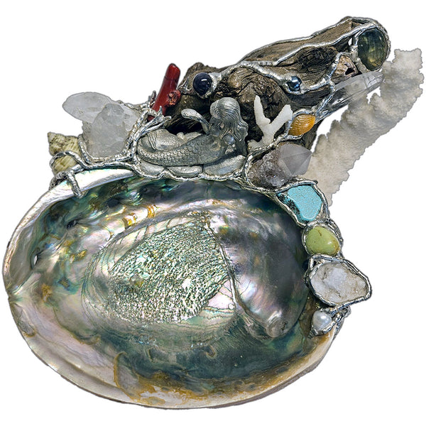 A mermaid rests on a large pink abalone shell, adorned with corals, seashells, gemstones and driftwood top view