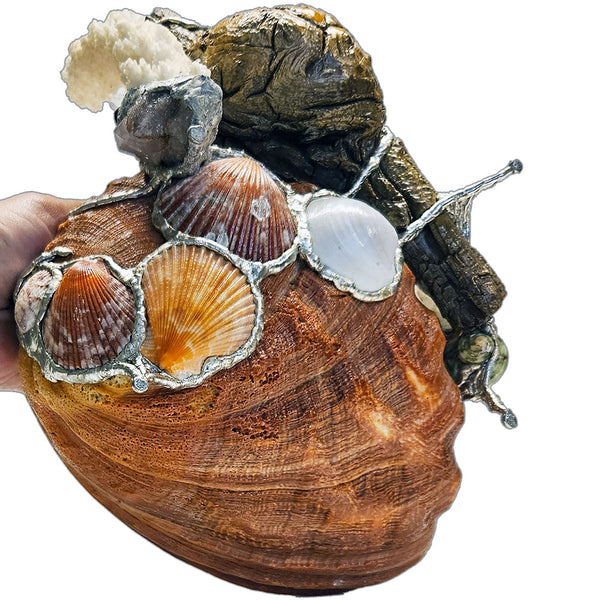 A mermaid rests on a large pink abalone shell, adorned with corals, seashells, gemstones and driftwood bottom view